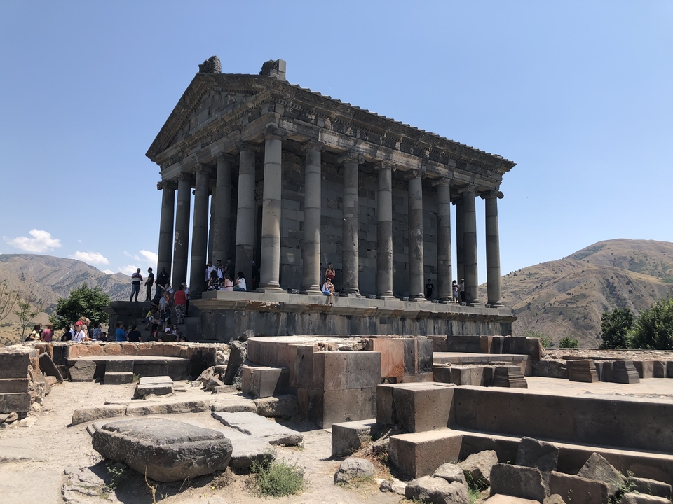Ancien temple de pierre avec colonnes et des gens autour.
