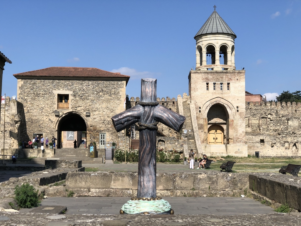 Forteresse en pierre avec une croix en bois devant et des gens à proximité.