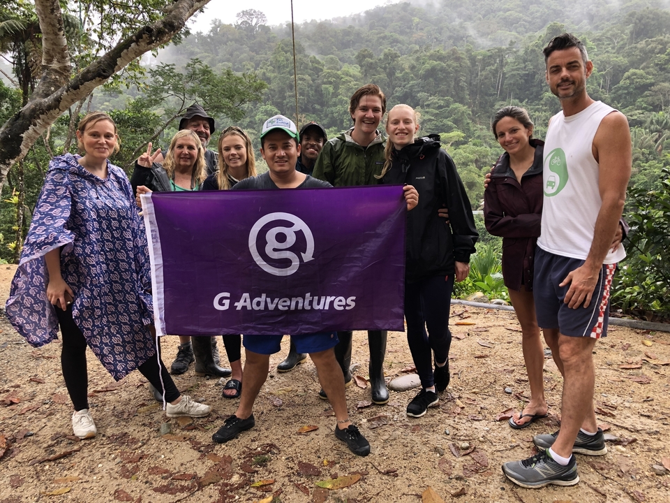 Groupe de personnes joyeuses tenant un drapeau d'aventure d'entreprise dans une jungle.