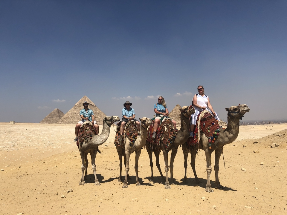 Touristes à dos de chameau avec les pyramides en arrière-plan.