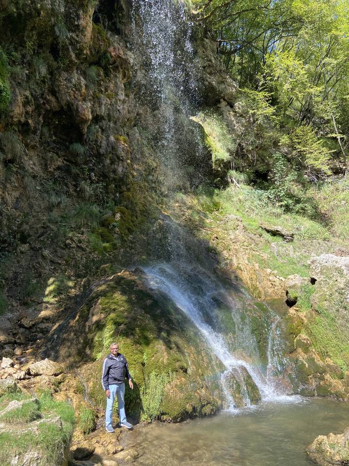 Wasserfall mit üppigem Grün und einer Person, die in der Szene steht.