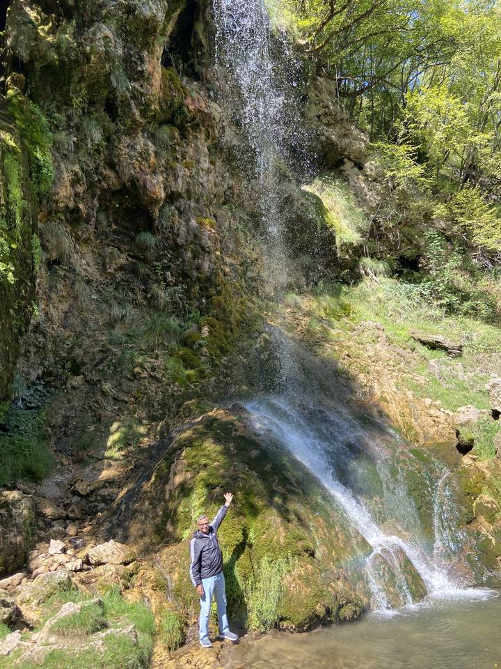 Wasserfall mit üppigem Grün und einer posierenden Person.