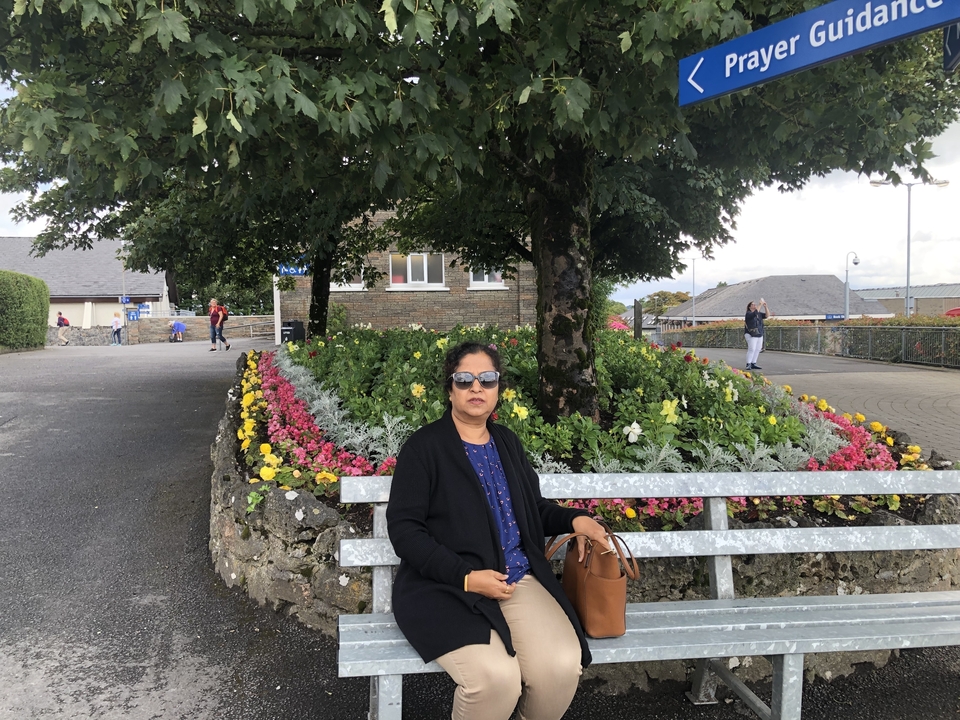 Personne assise sur un banc près de fleurs et d'arbres.