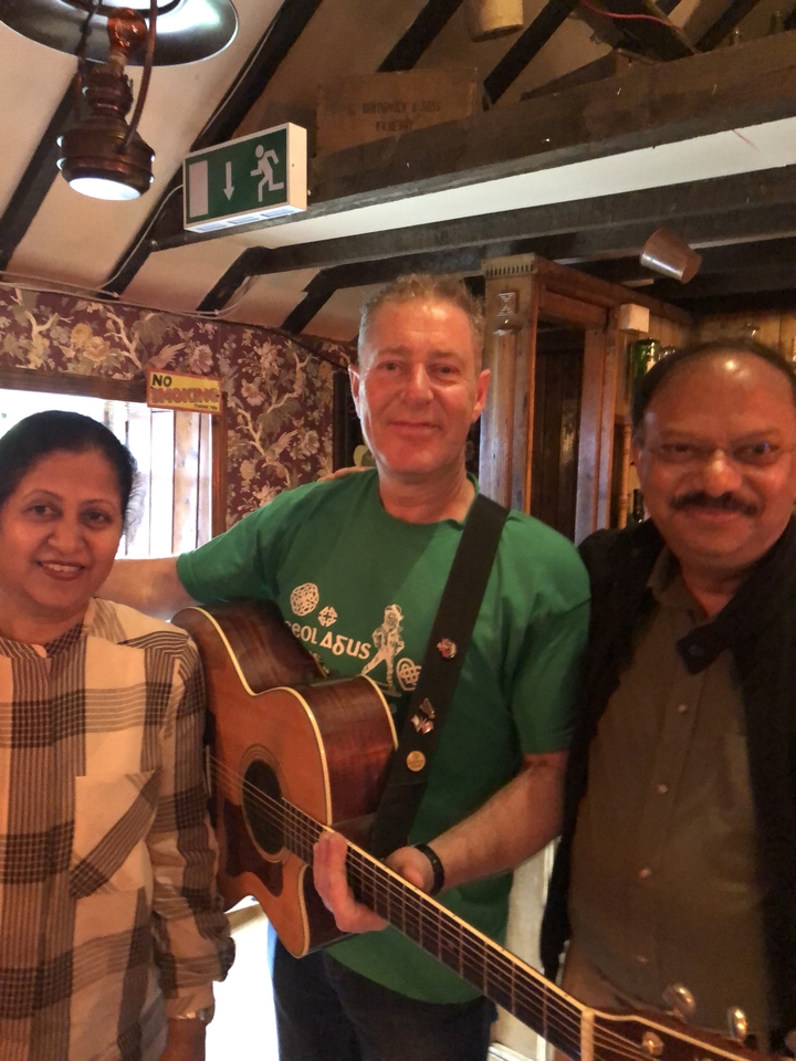 Trois personnes posant à l'intérieur d'un pub, une avec une guitare.
