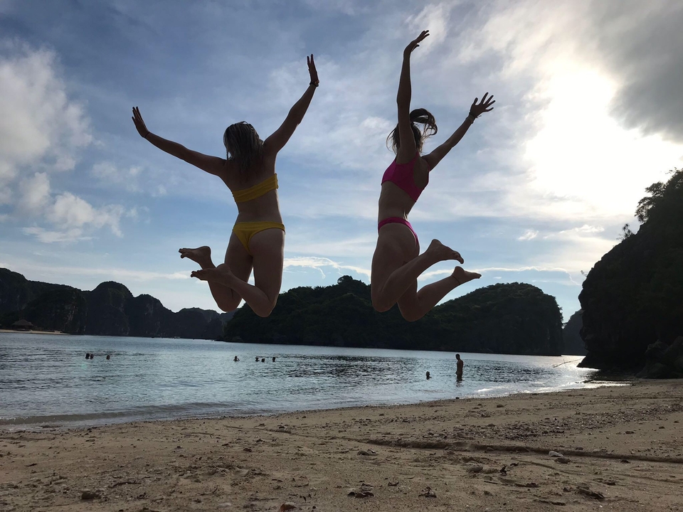 Dos mujeres saltando en el aire en una playa con una vista panorámica.