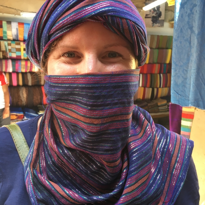 Une personne souriante portant une écharpe colorée dans un marché.