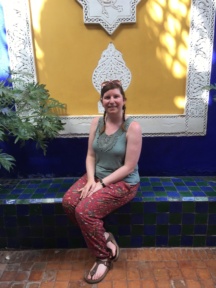 Une femme assise sur un sol carrelé coloré avec un décor en arrière-plan.