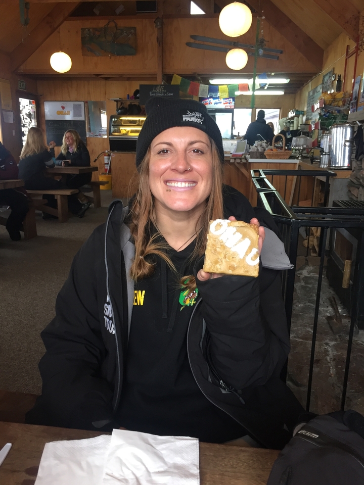 Une personne souriante tenant un morceau de rayon de miel dans un environnement intérieur.