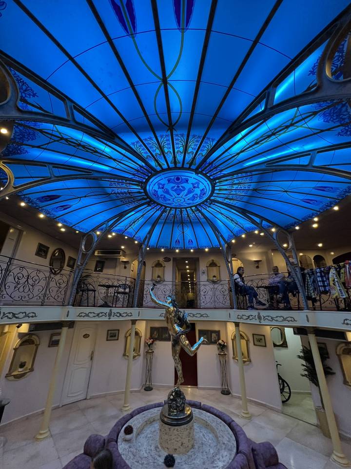 Interior with a blue stained glass dome ceiling and metal railings.