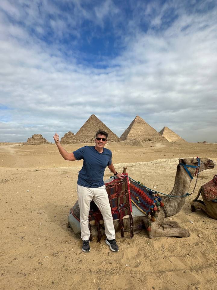 Personne assise sur un chameau avec des pyramides en arrière-plan.