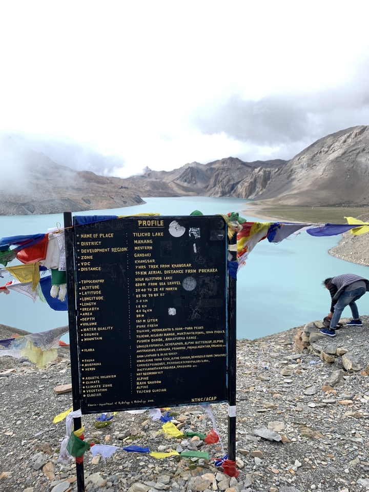 Signalisation avec le lac Tilicho en arrière-plan et des drapeaux de prière.
