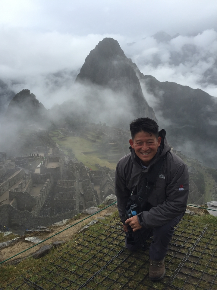 Smiling tourist with Machu Picchu in the foggy background.