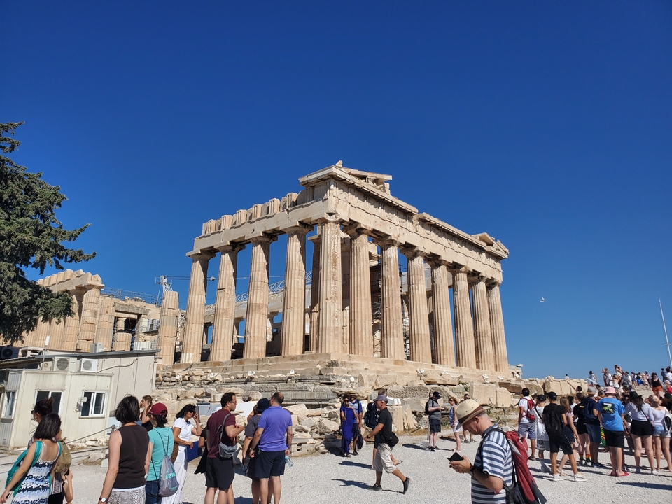 Des foules visitant le Parthénon à Athènes sous un ciel bleu dégagé.