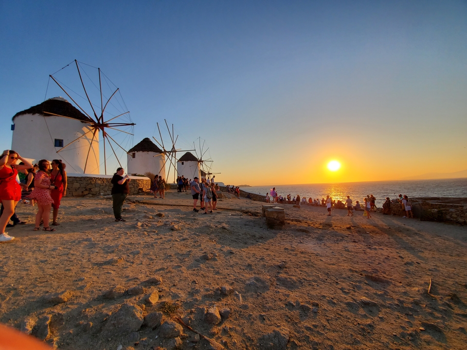 Des gens se sont rassemblés près des moulins à vent au bord de la mer pendant le coucher du soleil.