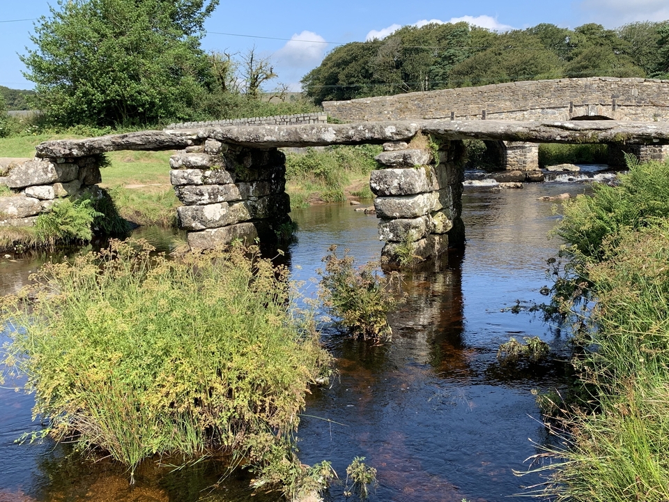 Pont à dalles de pierre traversant une rivière dans une zone pittoresque.