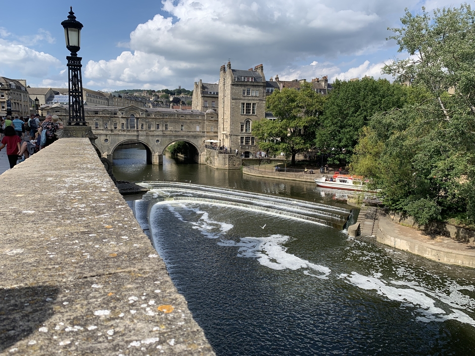 Pont au-dessus d'un déversoir dans une rivière avec de vieux bâtiments en arrière-plan.