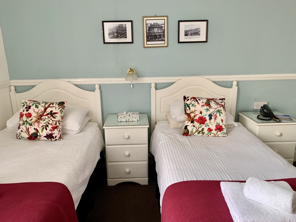 Deux lits simples avec des oreillers colorés dans une chambre bien éclairée.