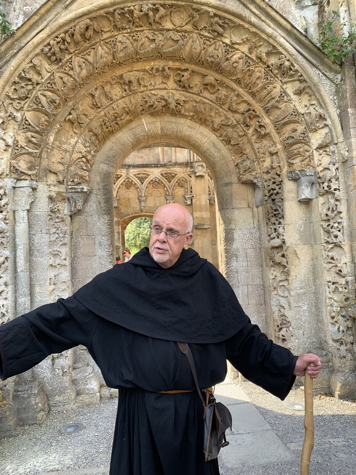 Homme en robe de moine se tenant dans une ancienne porte de pierre.