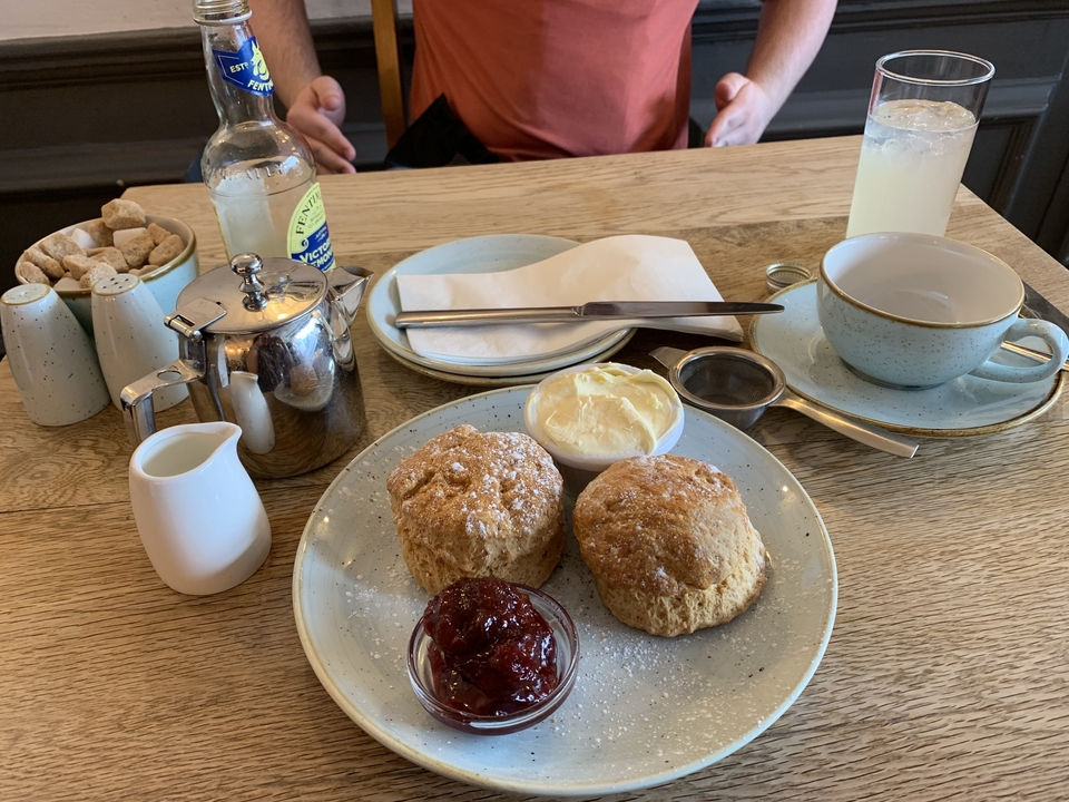 Table avec des scones, de la confiture et de la crème caillée, accompagnés de thé et de limonade.