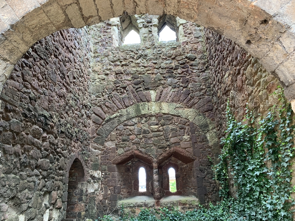 Intérieur d'une ruine en pierre avec des arches et des murs couverts de lierre.