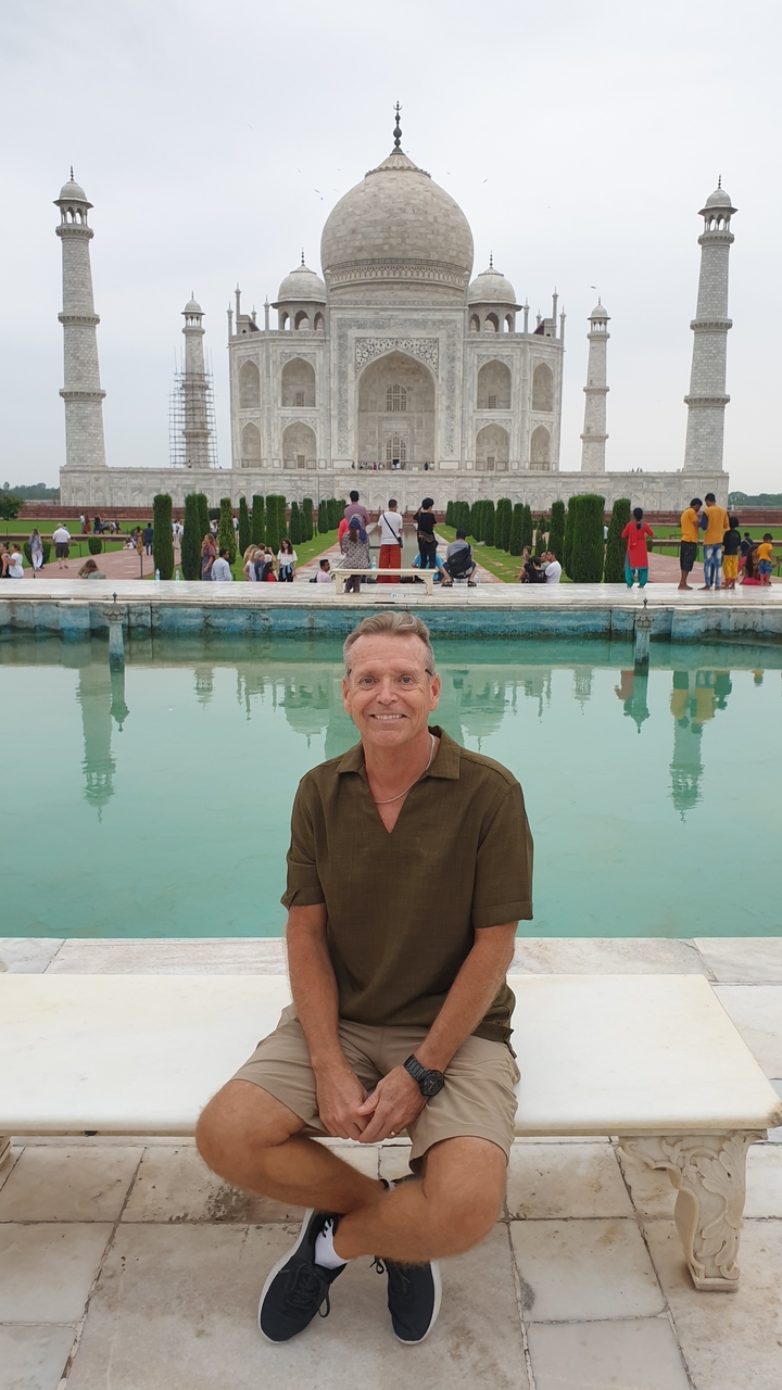 Homme posant devant une piscine avec une mosquée en arrière-plan.