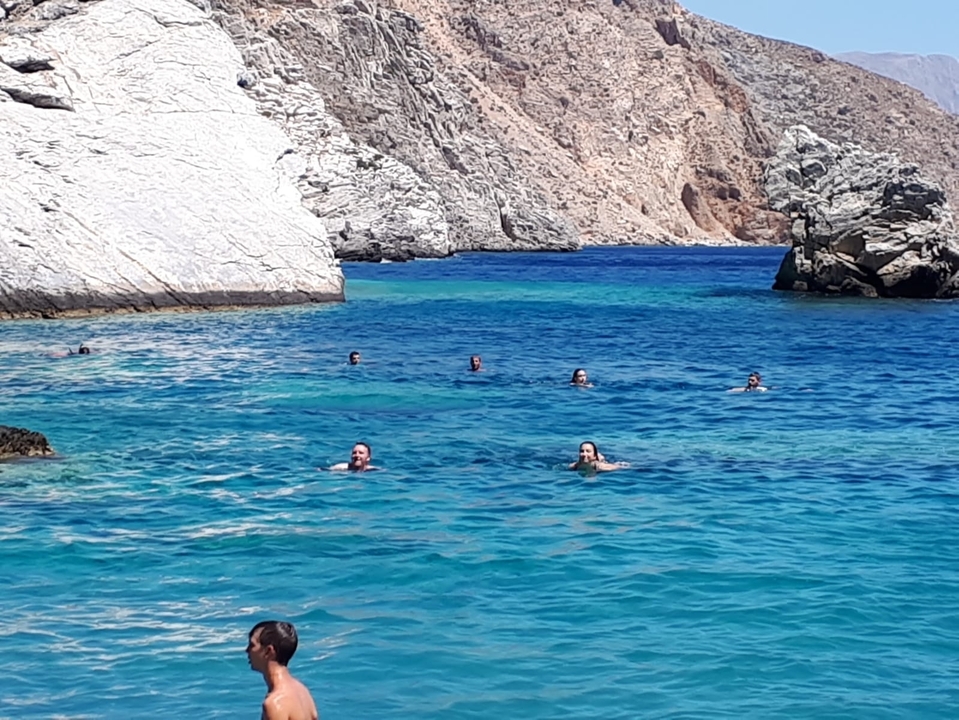 Des gens qui nagent dans des eaux bleues claires près de côtes rocheuses.