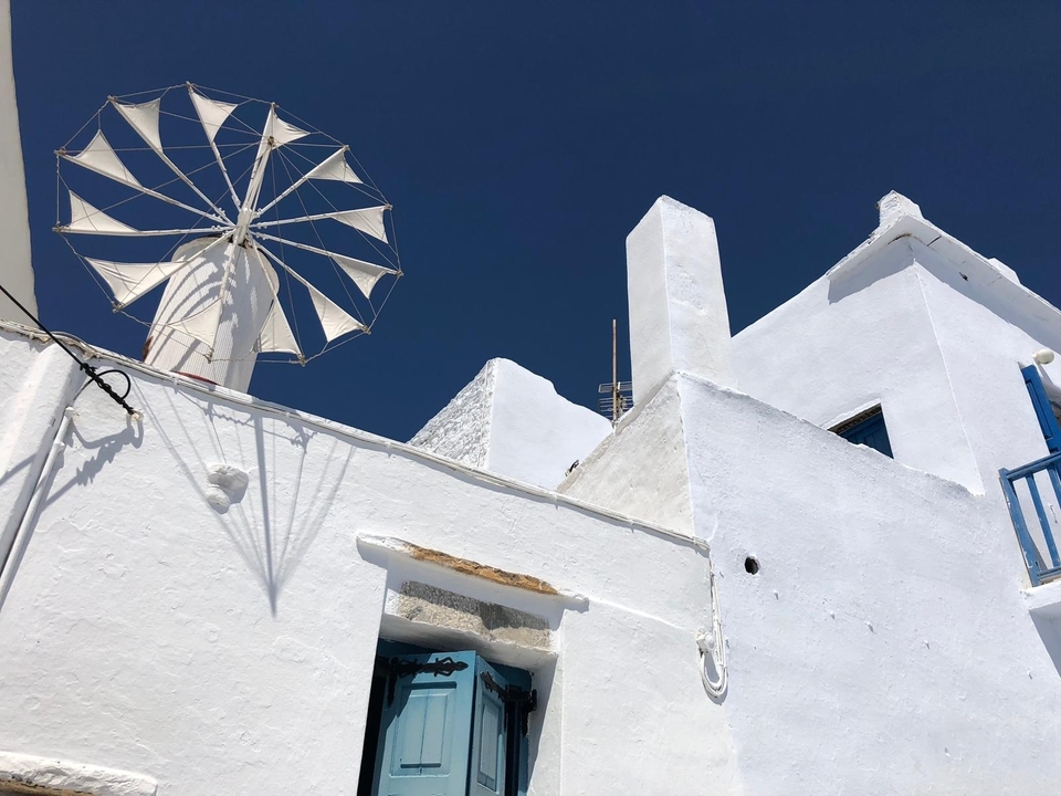 Bâtiments grecs traditionnels blancs avec un moulin à vent sous un ciel bleu.