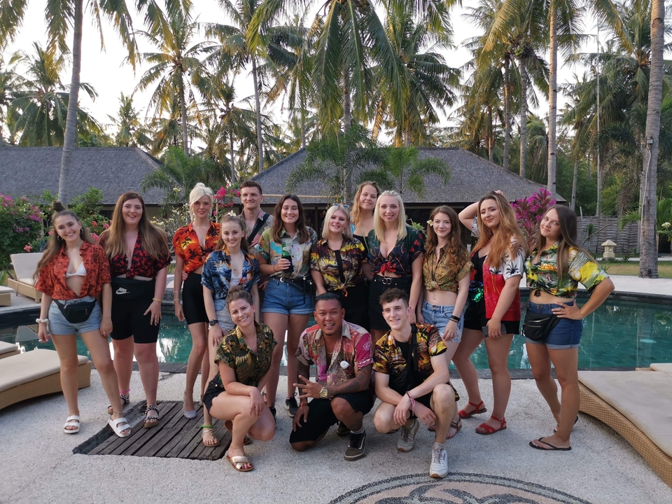 A large group posing by a pool with palm trees in the background.