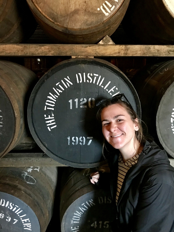 Personne souriante à côté d'un grand tonneau de distillerie.