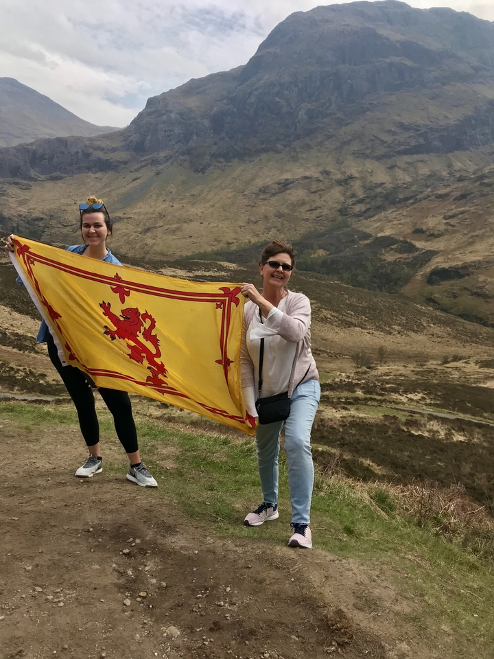 Deux personnes tenant un drapeau avec un emblème de lion dans un cadre extérieur pittoresque.