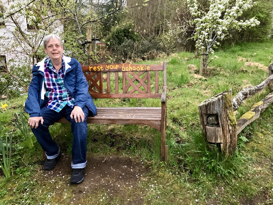 Personne assise sur un banc dans un jardin avec une inscription humoristique.