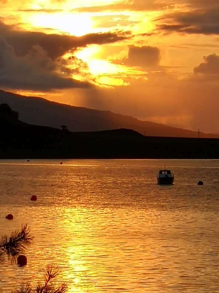 Un bateau sur un lac au coucher du soleil avec des montagnes en arrière-plan.