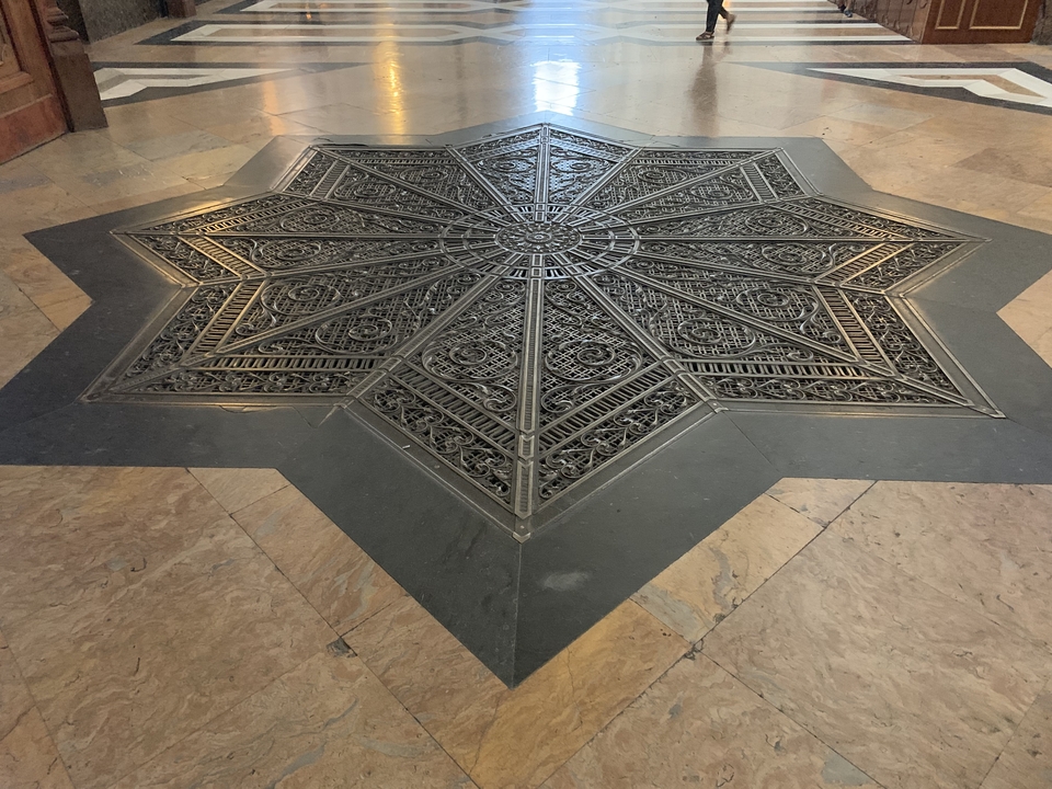 Motif géométrique complexe en métal incrusté dans un sol de marbre.