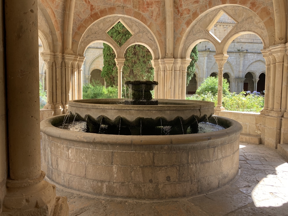 Fontaine en pierre dans une cour entourée d'arcs et de verdure.