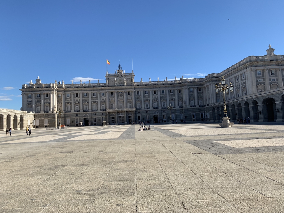 Palais royal avec une vaste cour d'honneur et des gens qui se promènent.