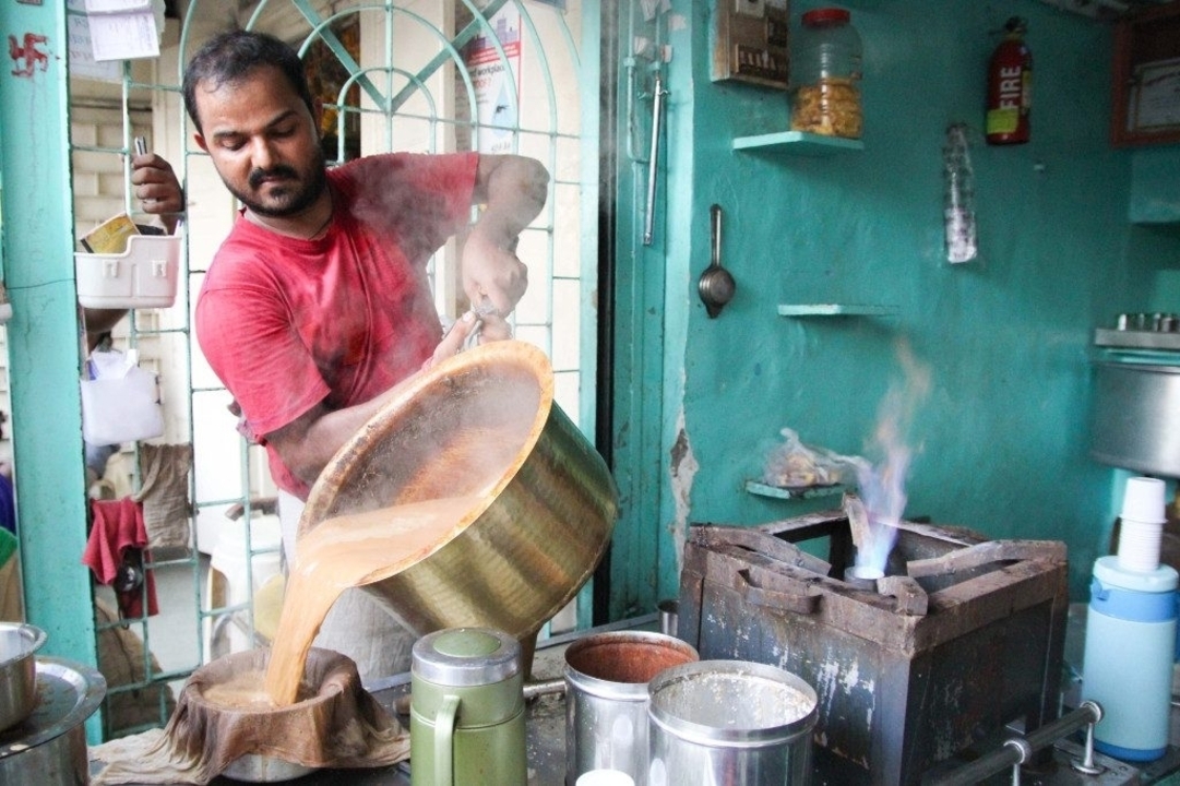 Marchand ambulant versant du thé chaud d'une grande bouilloire à l'intérieur.
