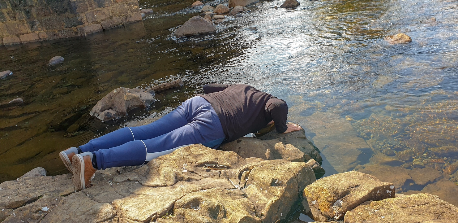 Personne buvant de l'eau d'un ruisseau.