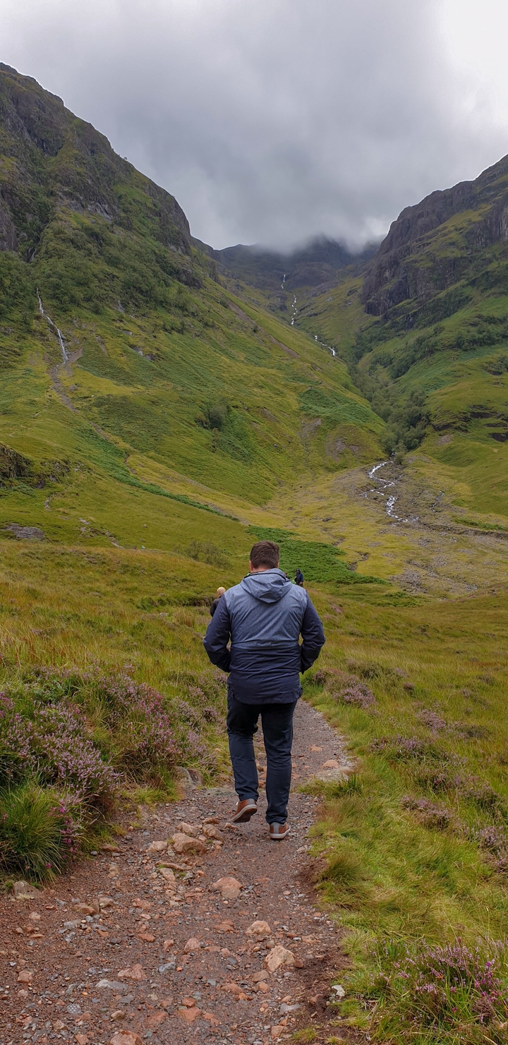 A person in a raincoat hiking in a green valley.