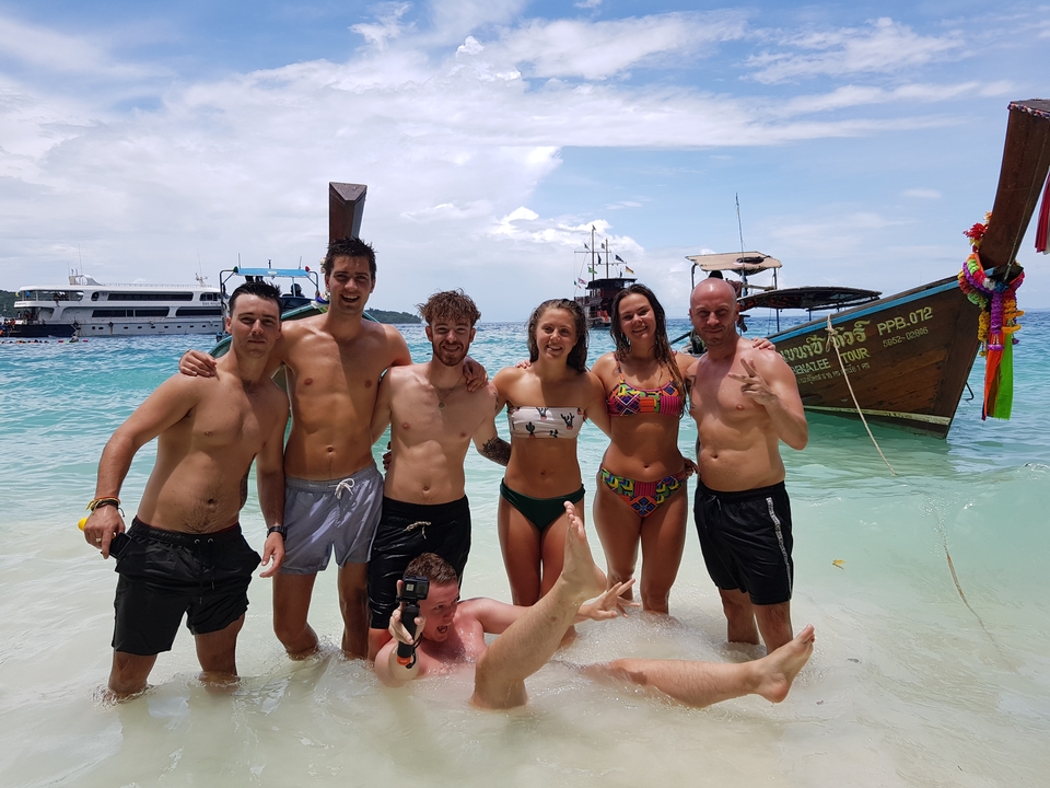 Group of people standing in the sea with boats in the background.