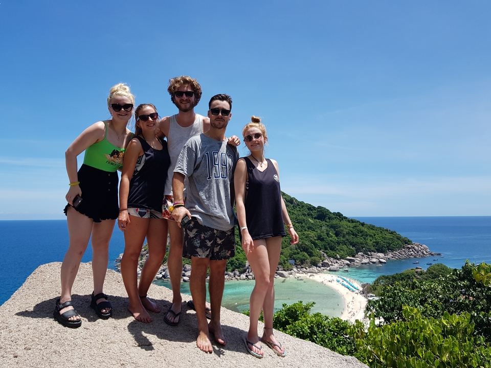Group of people posing on a rock with a scenic beach view.
