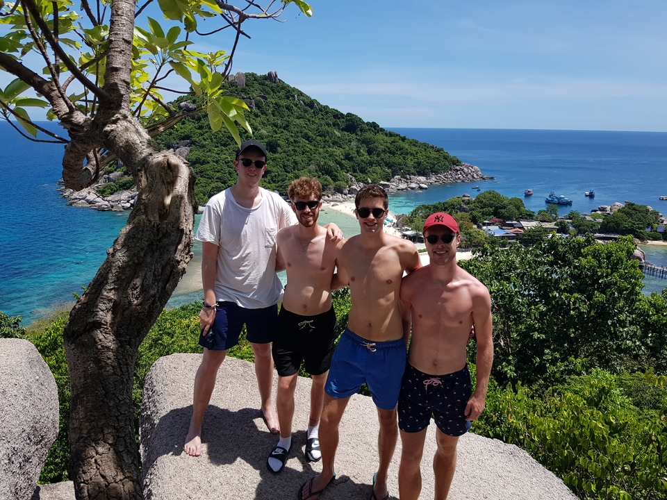 Four men posing on a rock with a beach view.