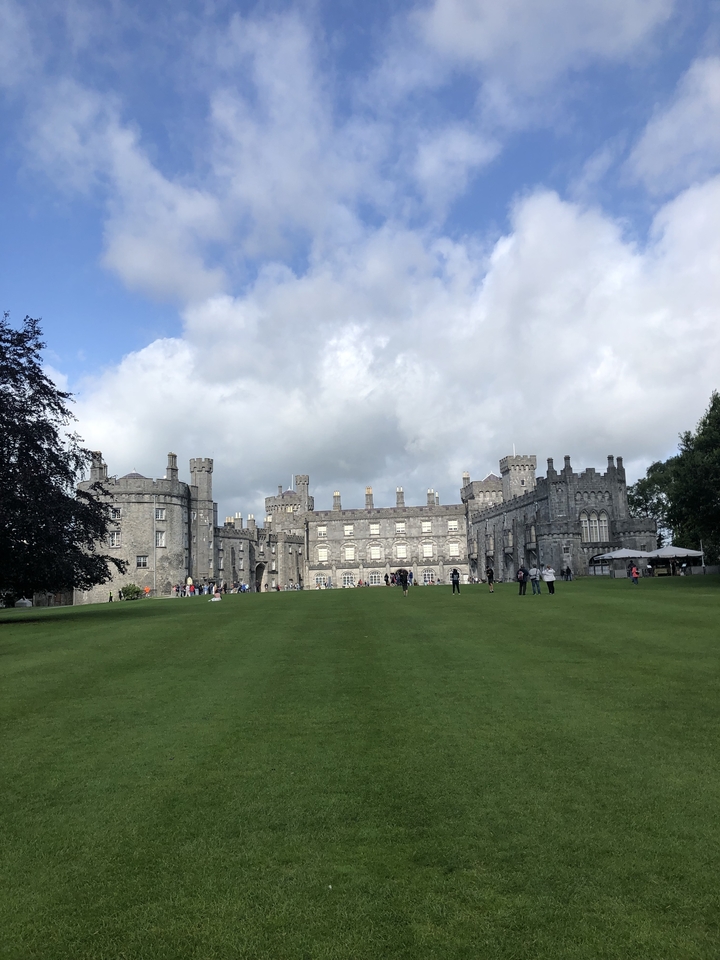 Grand château de pierre avec une pelouse verte et des touristes.