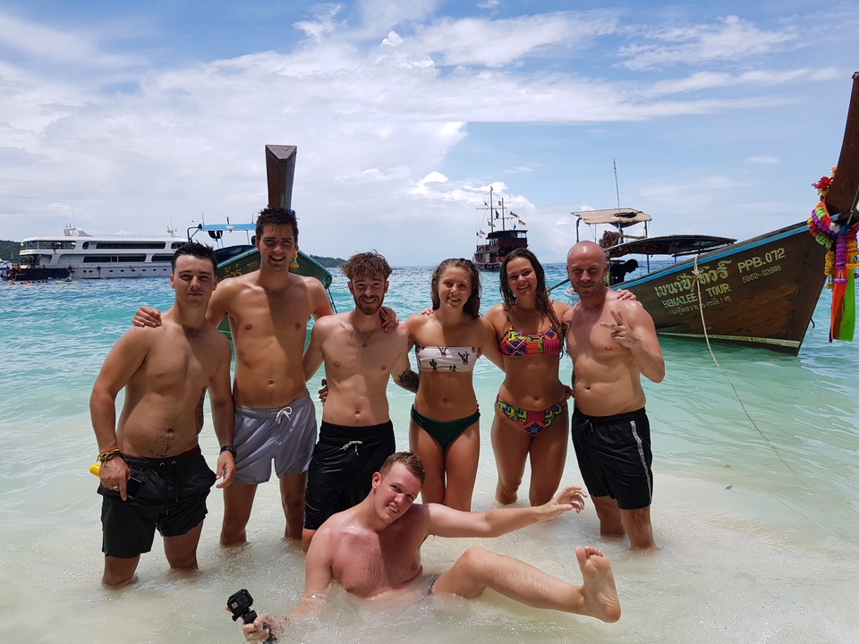 Group of people in the sea with boats in the background.