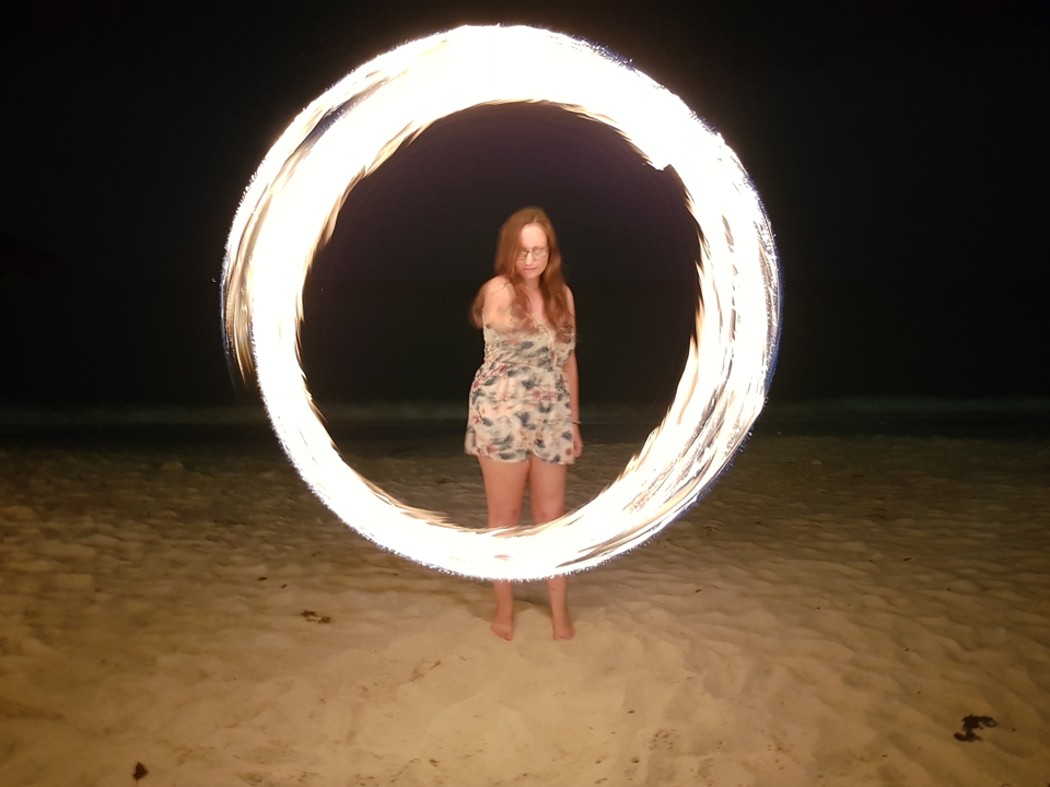 Personne faisant tourner du feu sur une plage la nuit.