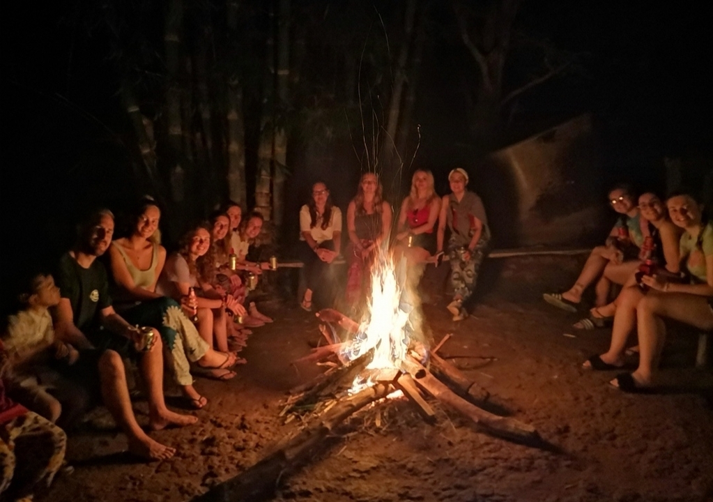Des gens assis autour d'un feu de camp la nuit.