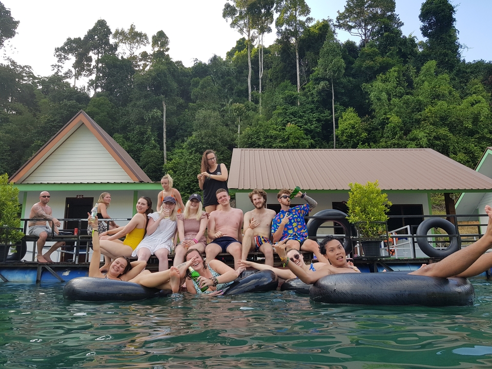 Groupe de personnes assises sur une plateforme flottante avec des maisons derrière.
