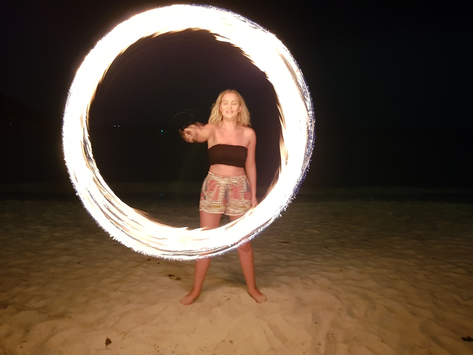 Femme faisant tourner un cerceau de feu sur une plage la nuit