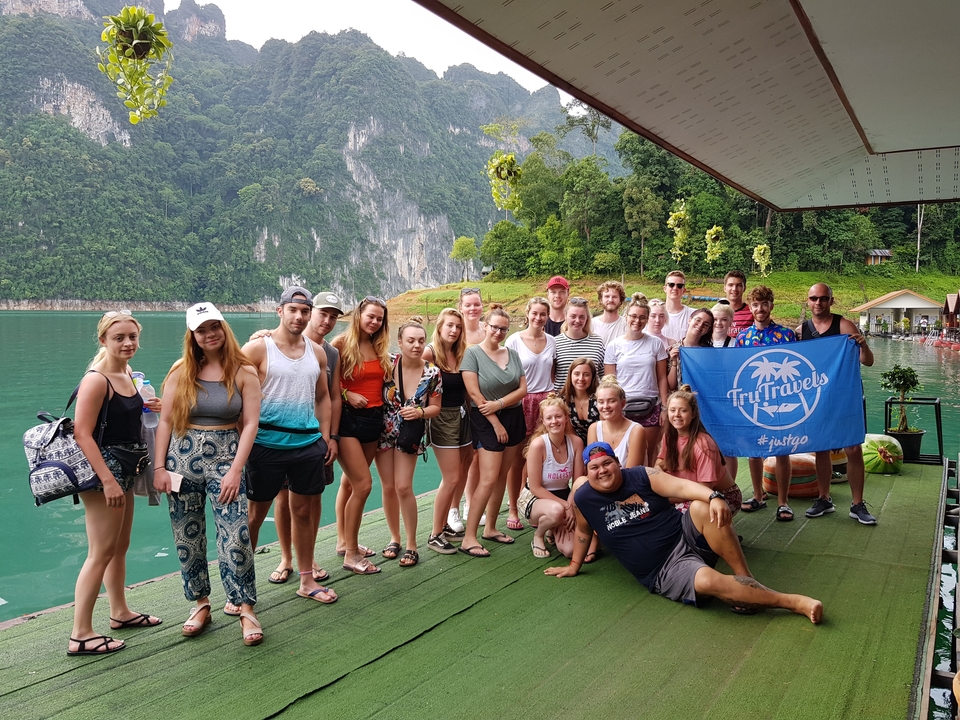 Groupe tenant un drapeau sur une plateforme au-dessus de l'eau avec des falaises en arrière-plan