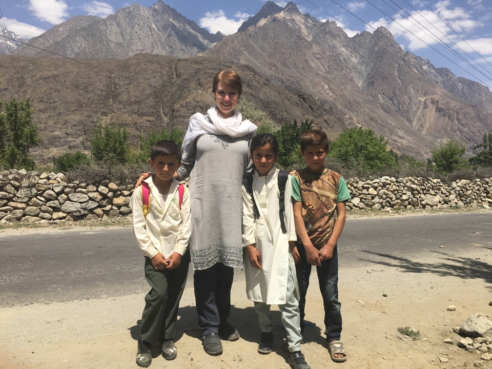 Une femme debout avec trois enfants au bord de la route avec des montagnes derrière.
