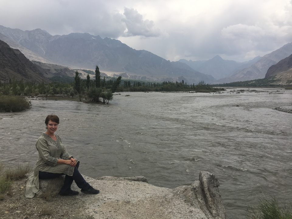 Une femme assise au bord d'une rivière avec des montagnes en arrière-plan.